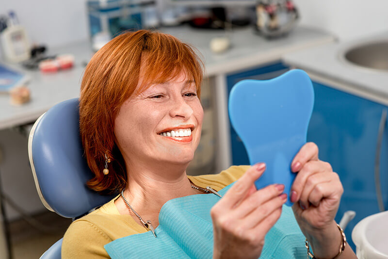middle aged-women on a dental chair with a hand mirror looking at her teeth